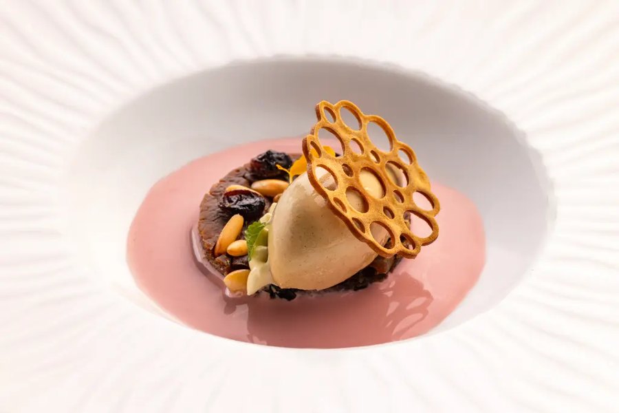 Un dessert coperto da una cupola di cialda dorata su fondo rosa