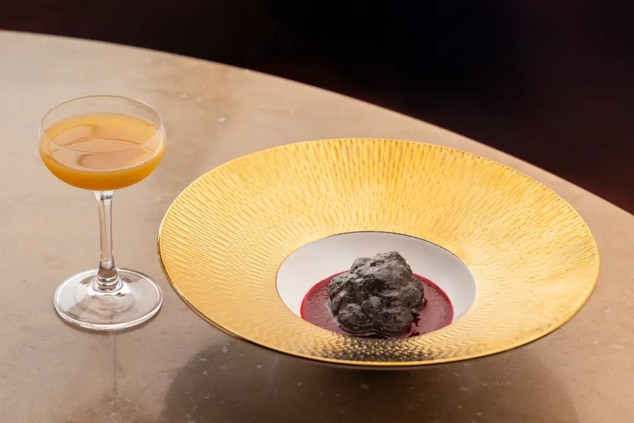 Un piatto su sottopiatto dorato accanto a una coppa da cocktail