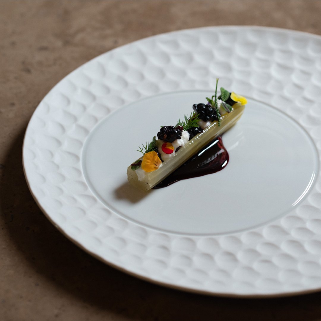 Un lingotto verde con more, agrumi e salsa scura su un piatto bianco