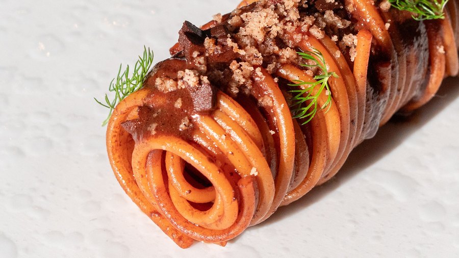 Una spirale di pasta arancione con crumble e aneto, vista di lato