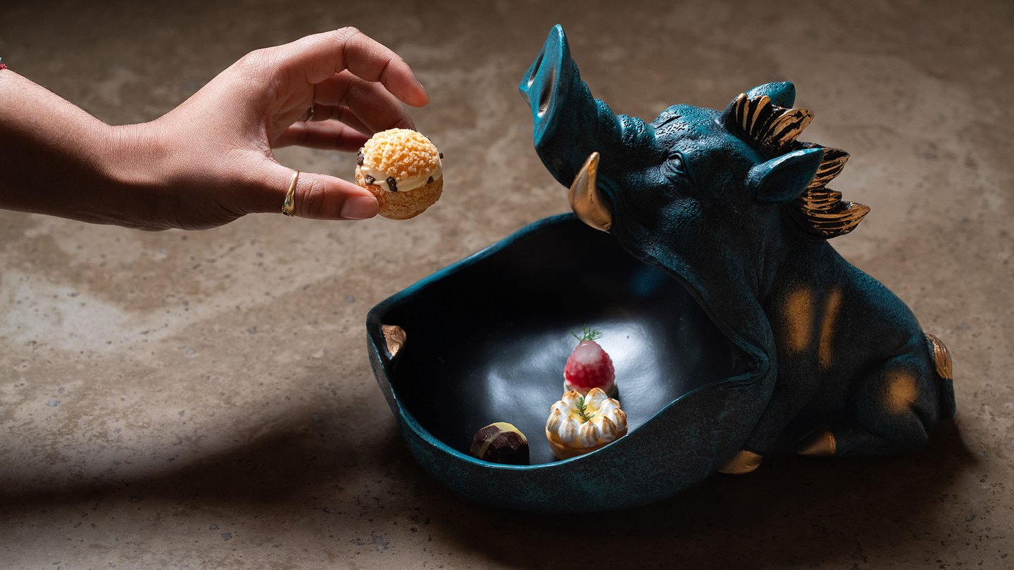 Un dessert servito dentro un toro di ceramica blu, con una mano che vi depone una sfera