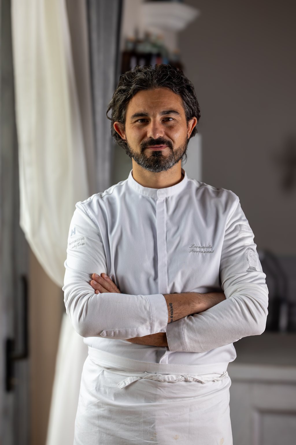 Leonardo Fiorenzani in giacca da cuoco JRE, braccia conserte, davanti a un quadro con fichi d’India