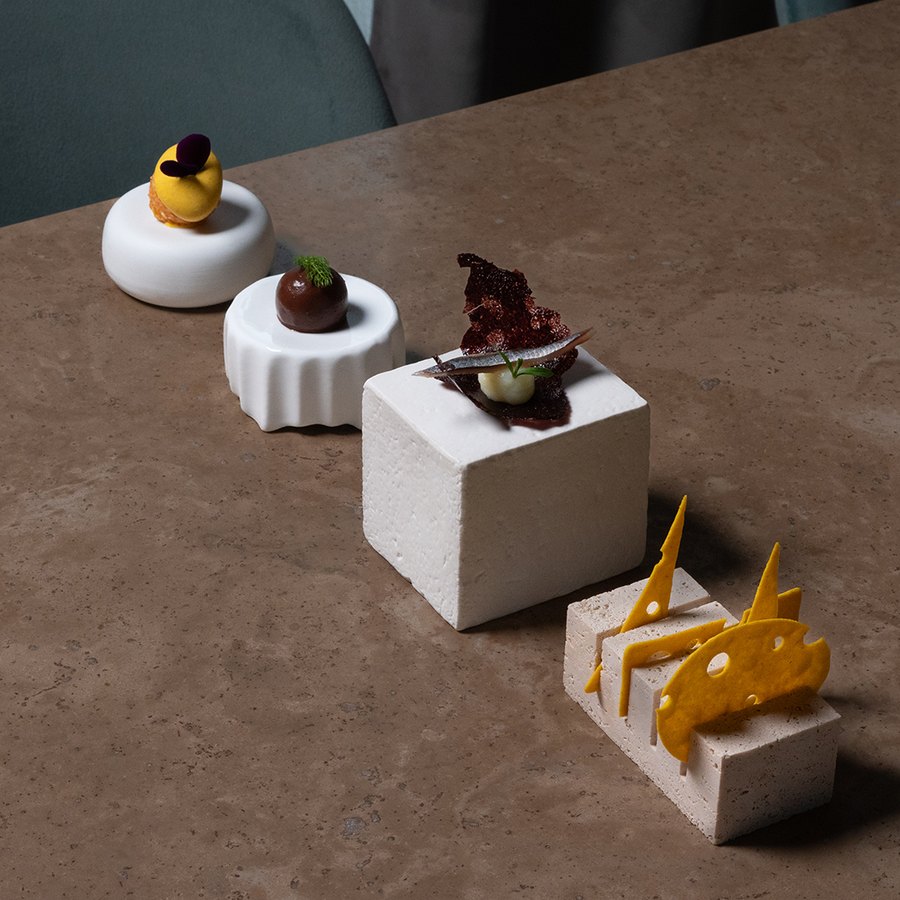 Opening bites arranged on three white stone cubes at different heights, with a shard of yellow sugar